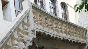 Un pati amb escales de pedra que condueixen a una entrada de building, plantes en testos i un mural.