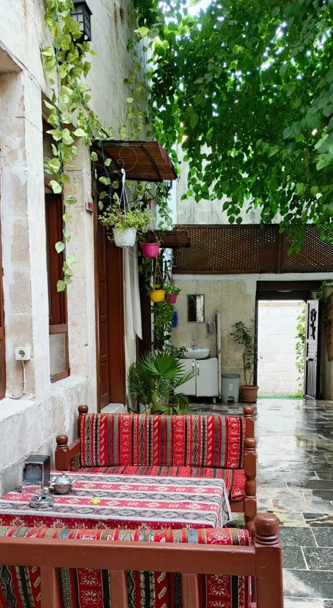 Een traditionele binnenplaats met een houten bank en tafel, omgeven door weelderige begroeiing en een rustieke stenen muur.