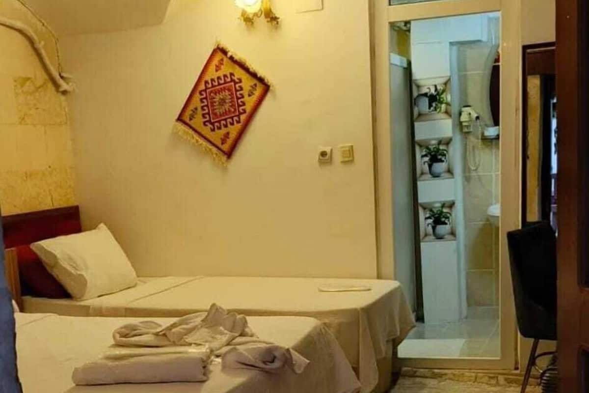 A bedroom with two beds, a stone floor, a small table, and a doorway leading to a bathroom.