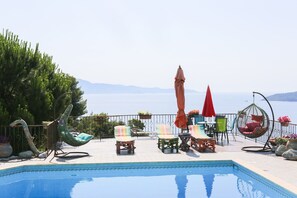 Zona de piscina con sillones, sombrillas y una silla colgante con vistas a un cuerpo de agua.