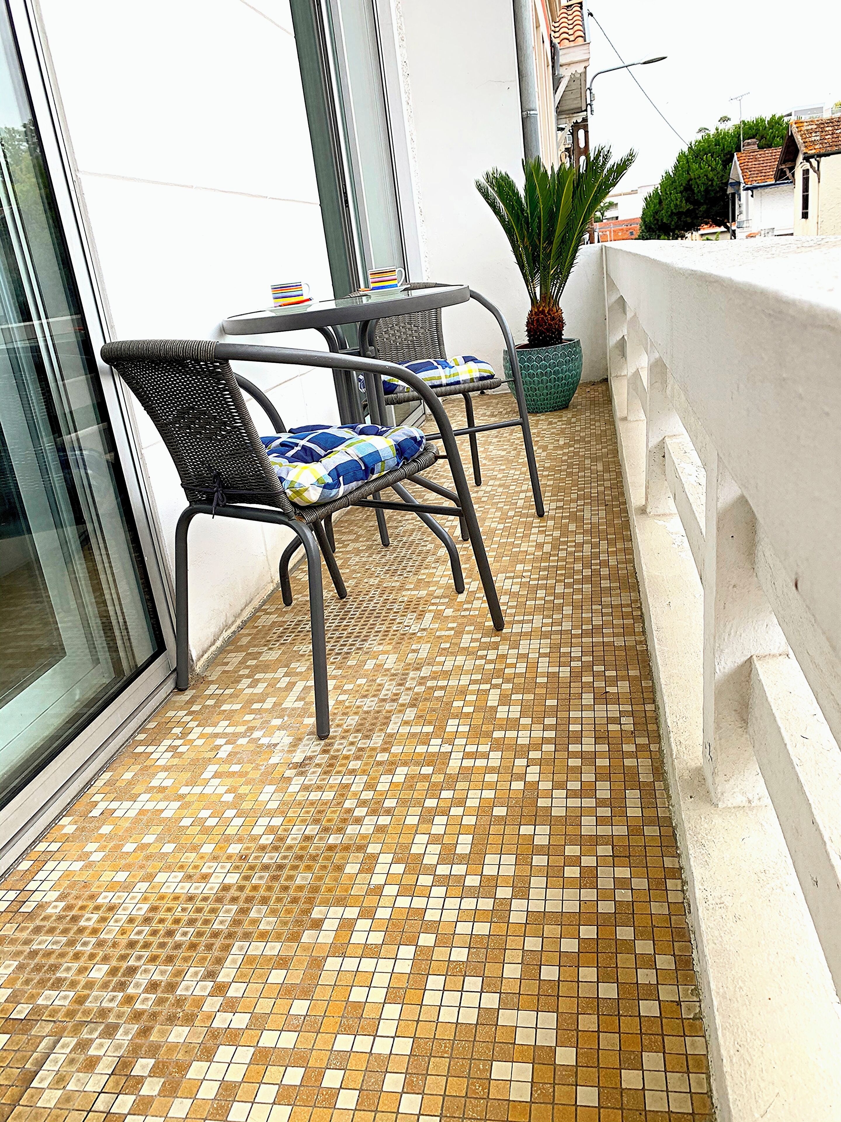 A small outdoor seating area with two chairs and a table, a tiled floor, and a potted plant.