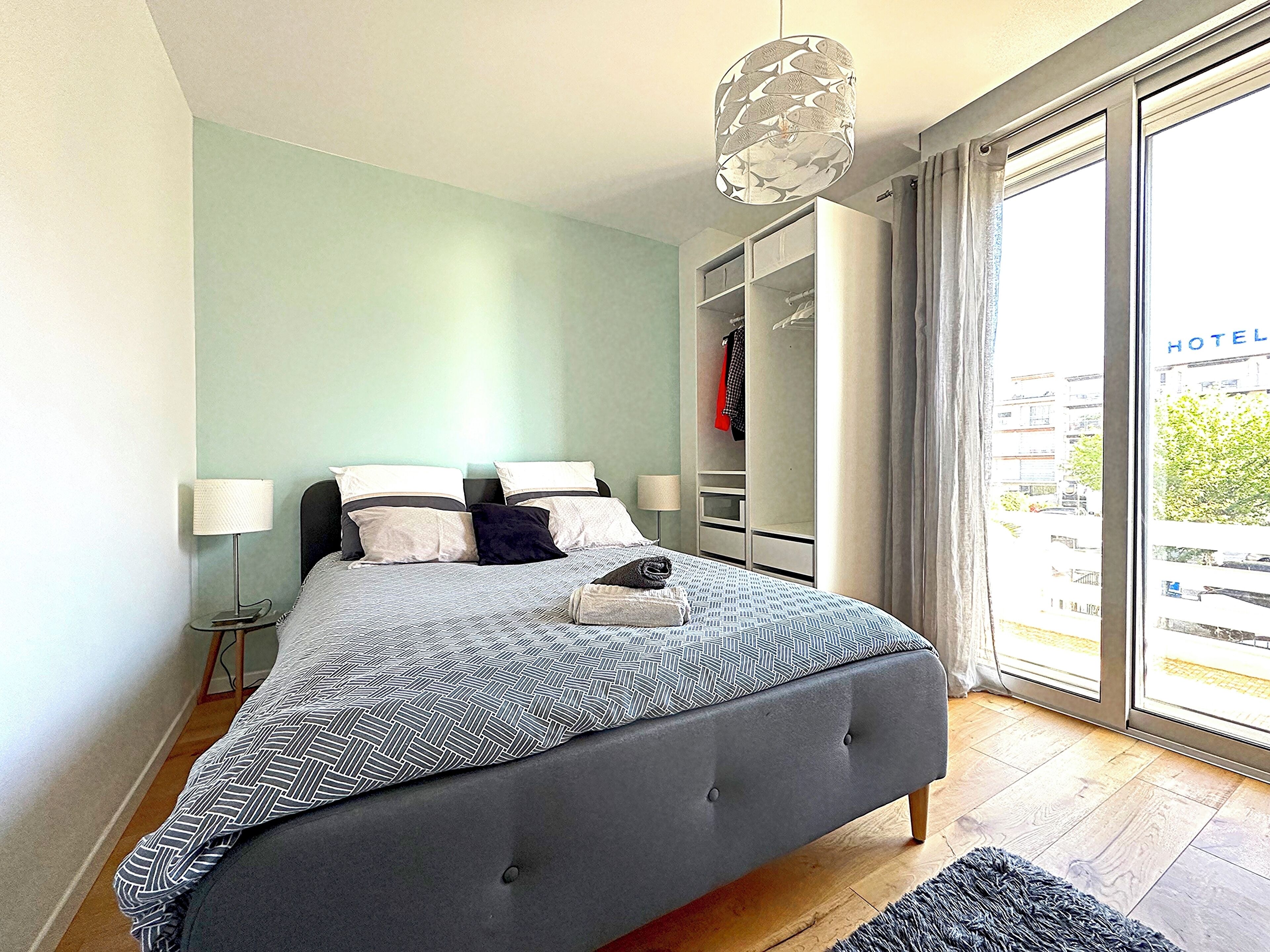Un dormitorio con cama, lámparas de noche, armario y vistas al exterior.