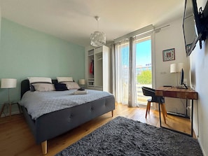 A bedroom with a bed, bedside lamps, a desk with a computer, and a view of the outside.
