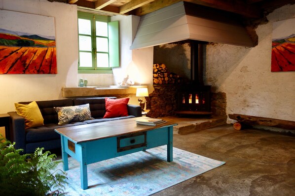 A cozy living room with a fireplace, a sofa with cushions, a coffee table, and artwork on the walls. - Beautiful, stylish and newly restored Watermill right on the river! (Ortigueira)