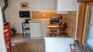 A compact kitchen with a stove, sink, and a small refrigerator. There is a wooden ceiling and a tiled backsplash.