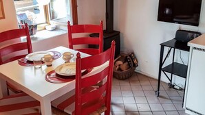 A dining area with a white table, red chairs, a lamp, a TV, and a fireplace.