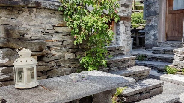 A stone bench with a lantern and teacups, set against a stone wall with a climbing plant.