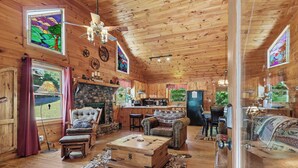 A wooden cabin interior with a stone fireplace, leather furniture, and a kitchen area. - LAKE BLUE RIDGE VIEW & ACCESS, POOL TBL, PROJECTOR, FIRE PIT, HOT TUB, DOGS OKAY (Blue Ridge)