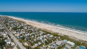 An aerial view of a coastal residential area with houses, a beach, and the ocean.