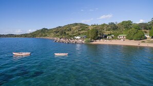 A coastal scene with clear blue water, two boats, a sandy beach, and houses on a hillside. - Ulisa Bay Lodge (Likoma Island)