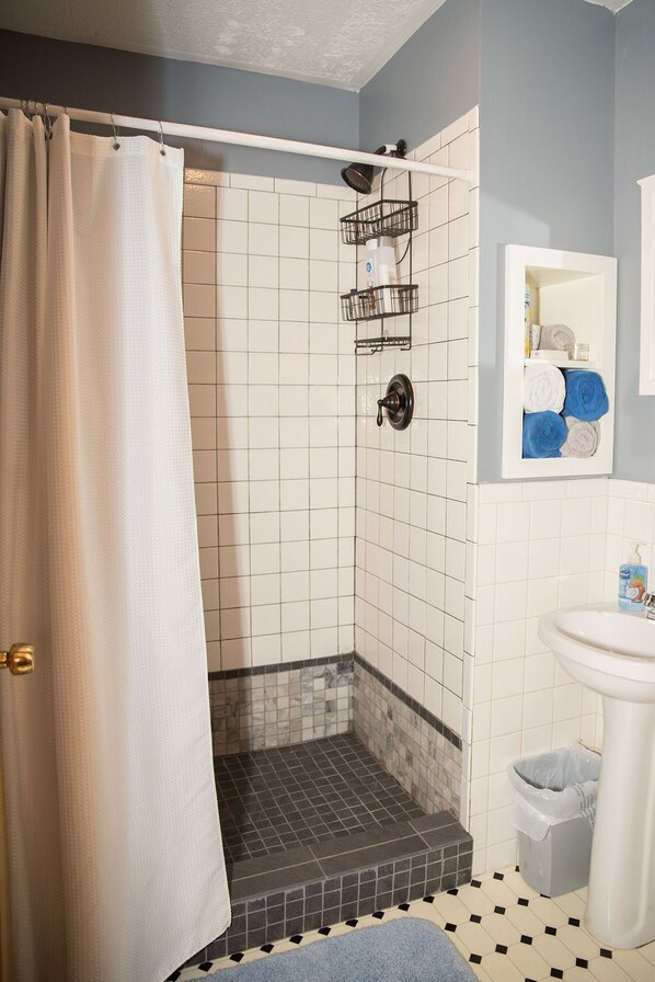 A bathroom with a shower, tiled walls, a sink, and a towel rack.