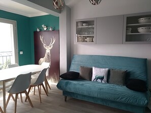 A modern living room with a teal sofa, a dining table with chairs, and a wall-mounted shelf with decorative items. - Beautiful apartment with balcony and panoramic views of the mountains (Font-Romeu-Odeillo-Via)
