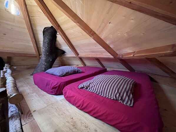 A small attic bedroom with two beds, wooden beams, and a sloped ceiling.