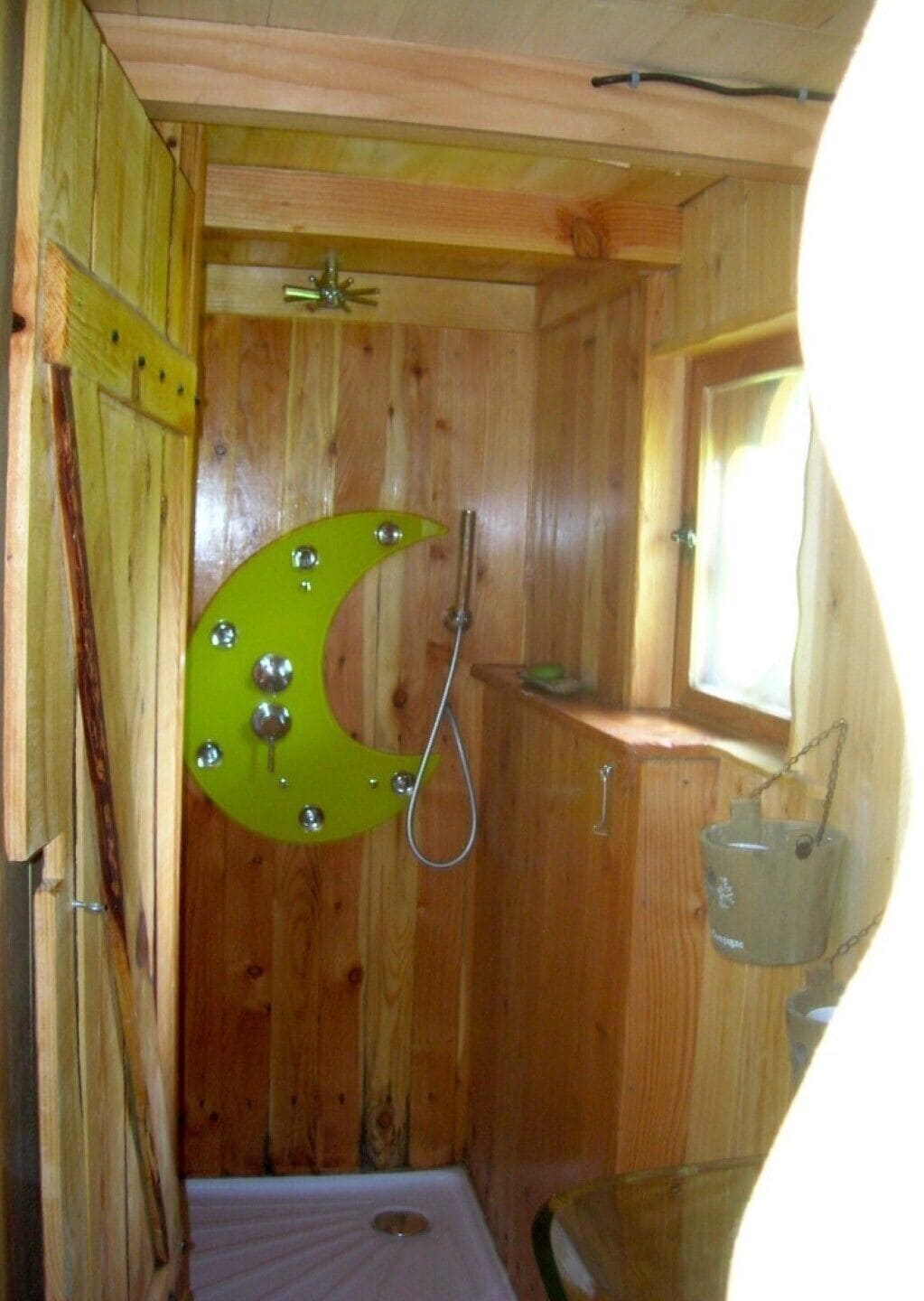 Ein Holzblockhaus-Interieur mit Duschbereich, kleinem Fenster und einem Metallkübel.