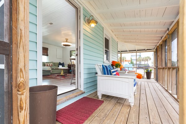 A covered porch with a white bed, a red rug, and a wooden bench.