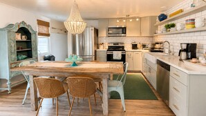 Une cuisine avec une table en bois, des chaises en osier, un lustre et des meubles de cuisine blancs.