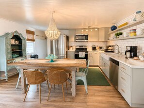 A kitchen with a wooden table, wicker chairs, a chandelier, and white cabinetry.