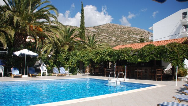 Una piscina con sillas de descanso, palmeras y una montaña al fondo.