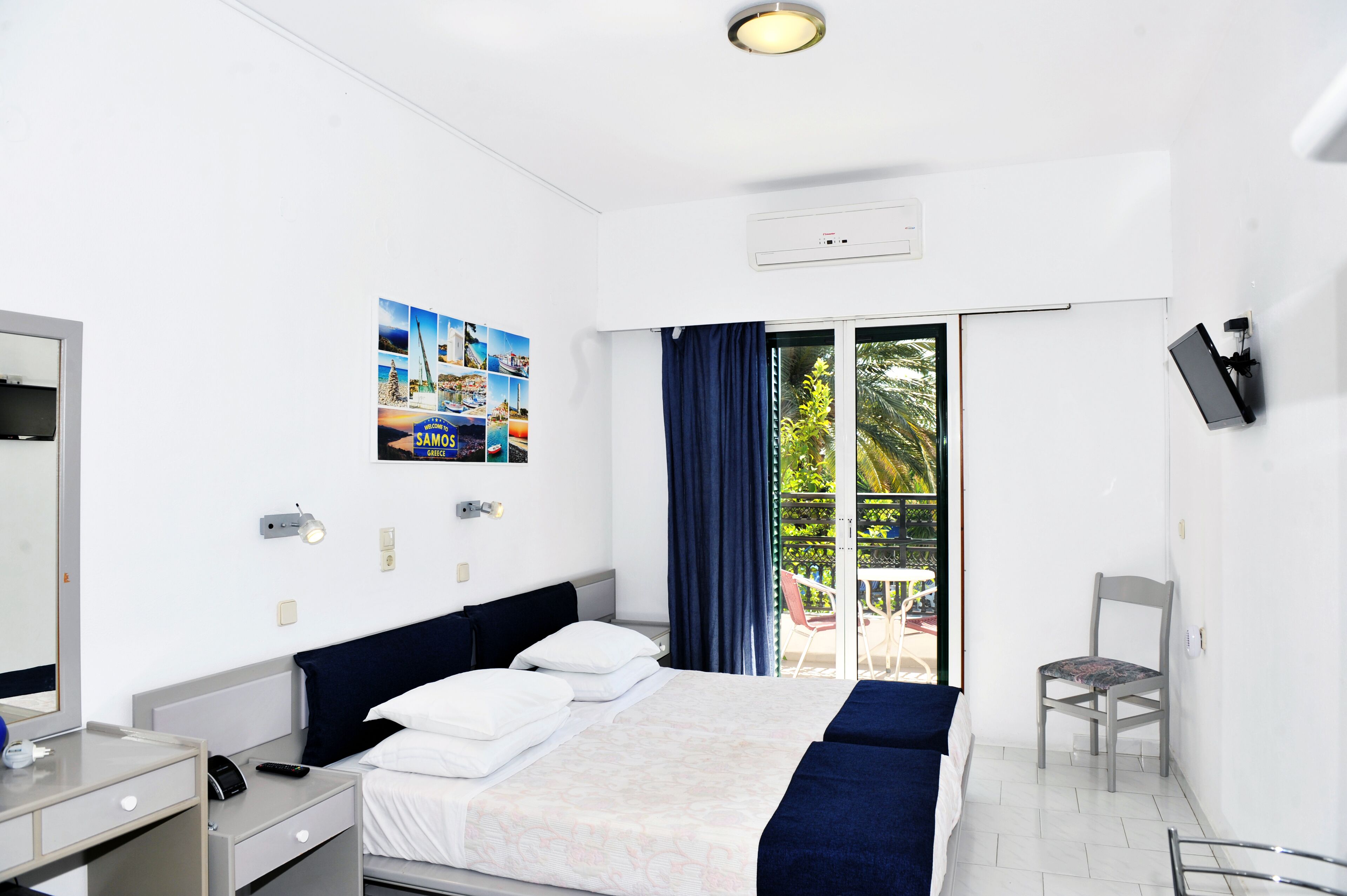 Une chambre d’hôtel équipée d’un lit, d’un bureau, d’une chaise, d’une télévision et d’un balcon donnant sur un paysage verdoyant.