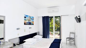 Habitación de hotel con cama, escritorio, silla, televisor y balcón con vistas a zonas verdes.
