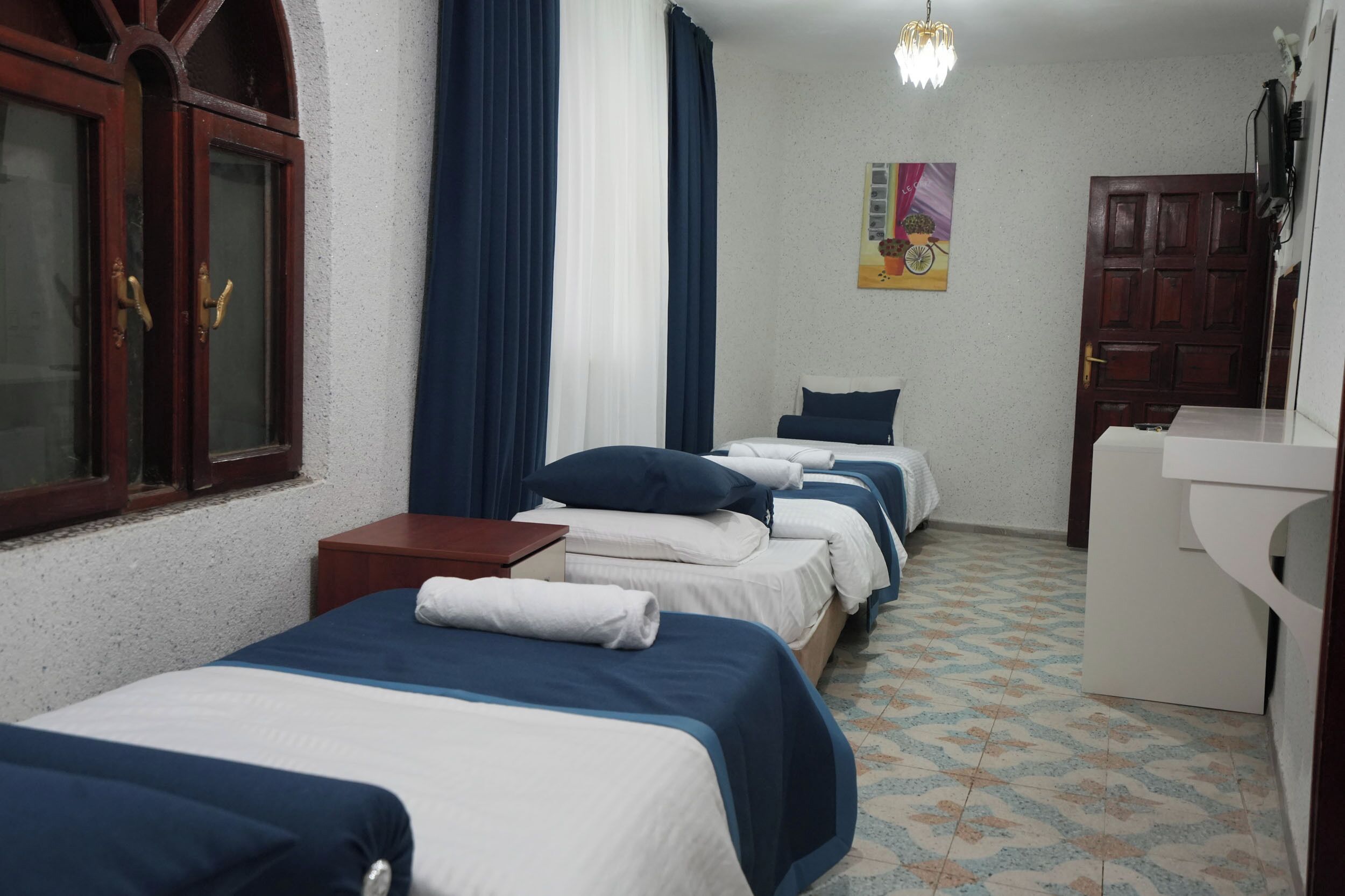 Una habitación de hotel con tres camas, un armario de madera, una mesita pequeña y un baño con lavamanos.