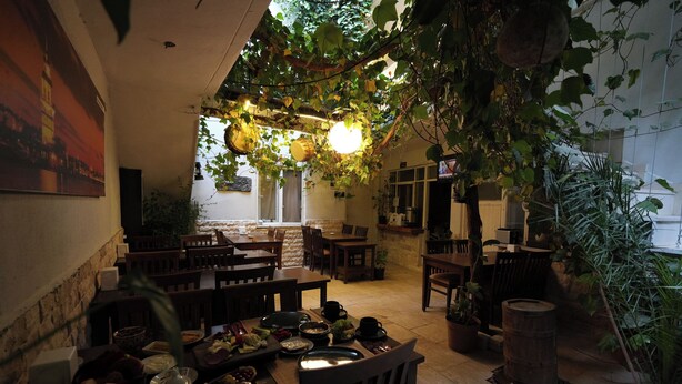 An indoor dining area with wooden tables and chairs, potted plants, and hanging plants. - Ozen Turku Hotel (Denizli)