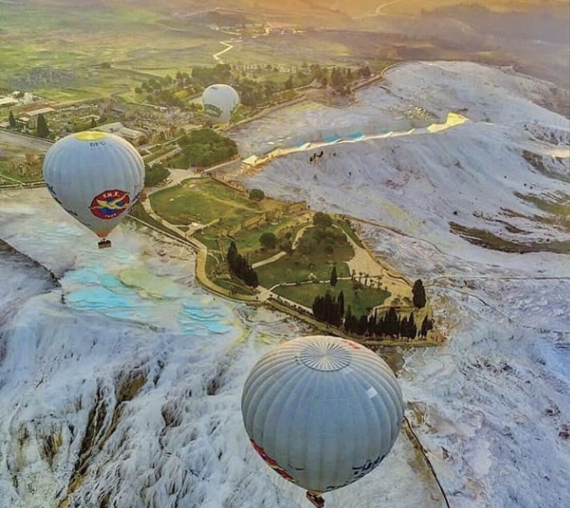Voo de balão de ar quente sobre uma paisagem montanhosa com rio e parque.