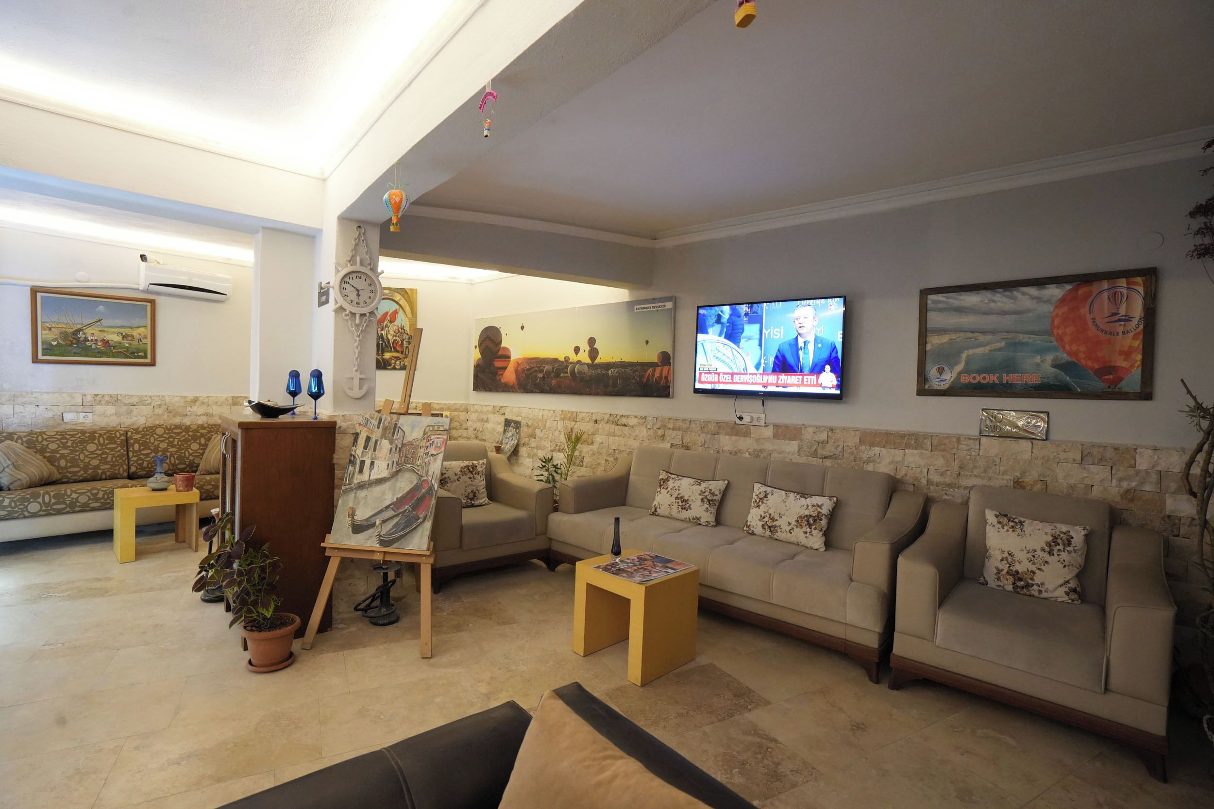 Una sala de estar con un sofá, una mesa de centro, un cuadro sobre caballete, un televisor y un reloj en la pared.
