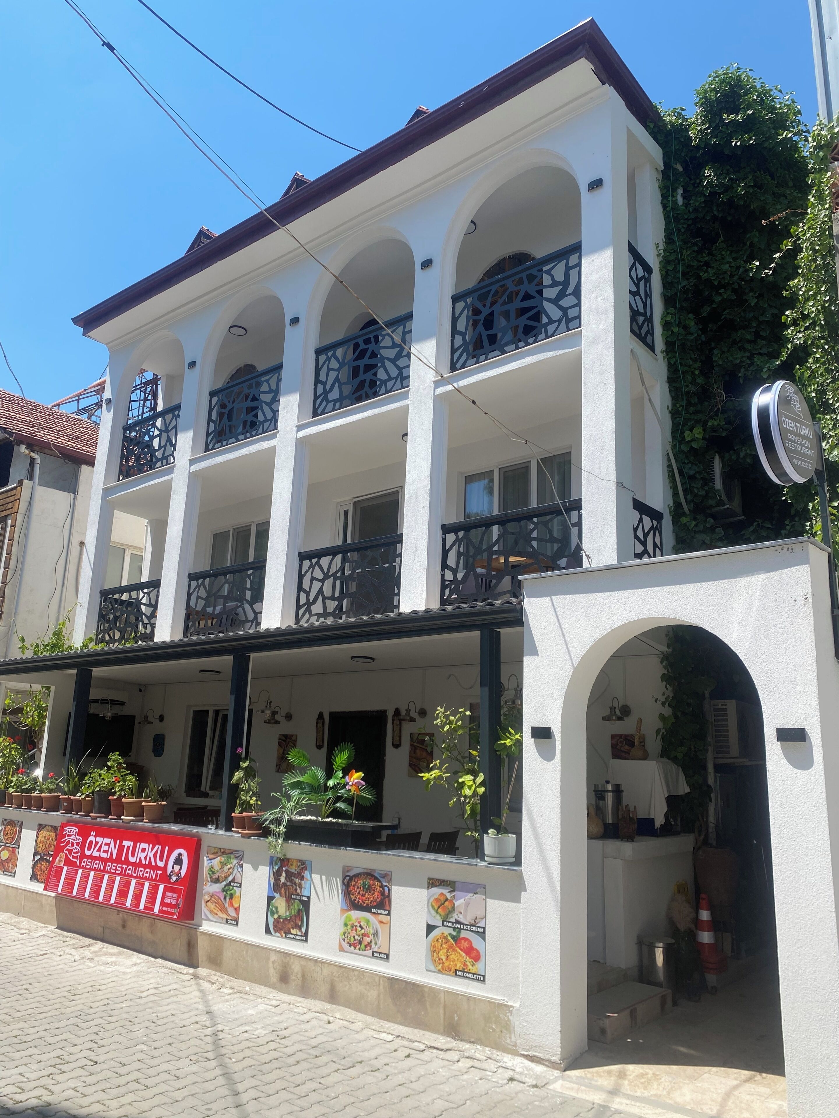 A two-story building with balconies, a sign for 'OZEN TURKU ASIAN RESTAURANT,' and potted plants on the ground floor.