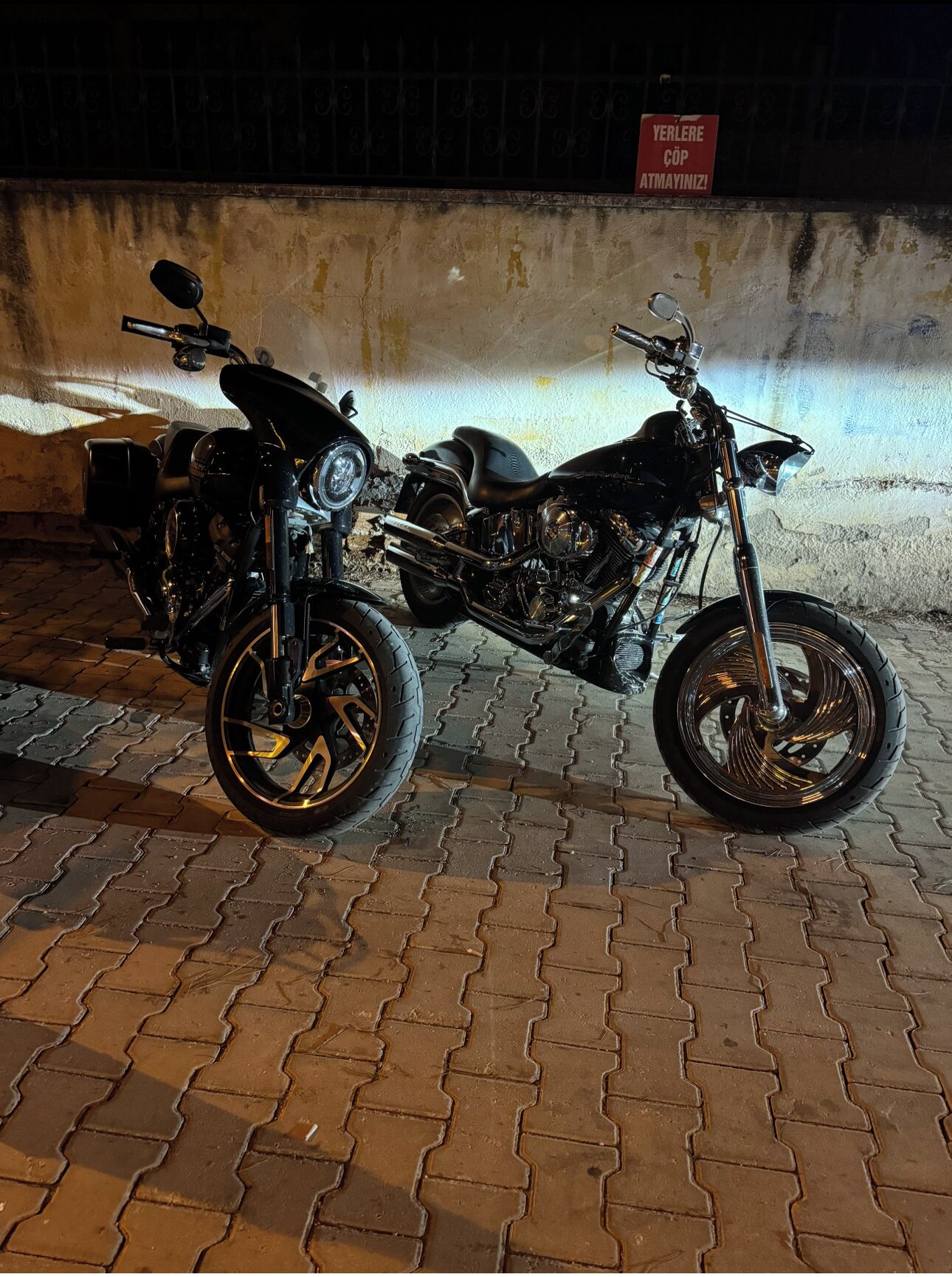 A motorcycle parked on a paved surface with a wall and a sign in the background.