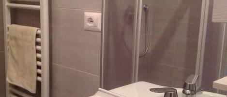 A bathroom with a white sink, a glass shower enclosure, and a towel rack with a towel.