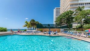 A swimming pool with clear blue water, surrounded by lounge chairs and palm trees.
