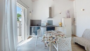 A compact kitchen with a microwave, stove, and refrigerator. There is a dining table with chairs and a sofa in the living area.