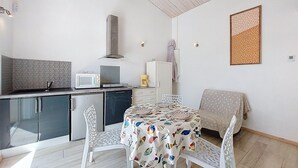 A compact kitchen with modern appliances, a dining area with a patterned tablecloth, and a decorative wall piece.