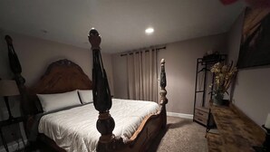 A bedroom with a wooden four-poster bed, a nightstand, a desk, and a chair.