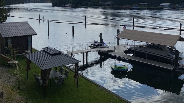 A riverside dock with boats, a small wooden building, and a grassy area with a fire pit.