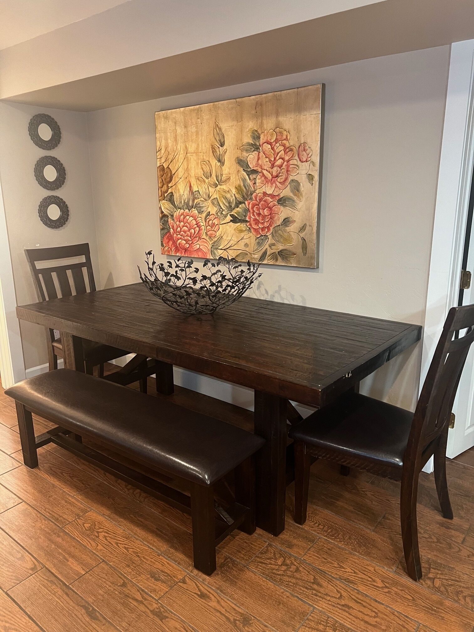 A dining area with a wooden table, benches, and a floral painting on the wall.