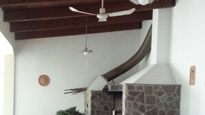 An outdoor patio with a stone fireplace, wooden benches, and ceiling fans. - THE TERRACE ON THE PARK (Oristano)