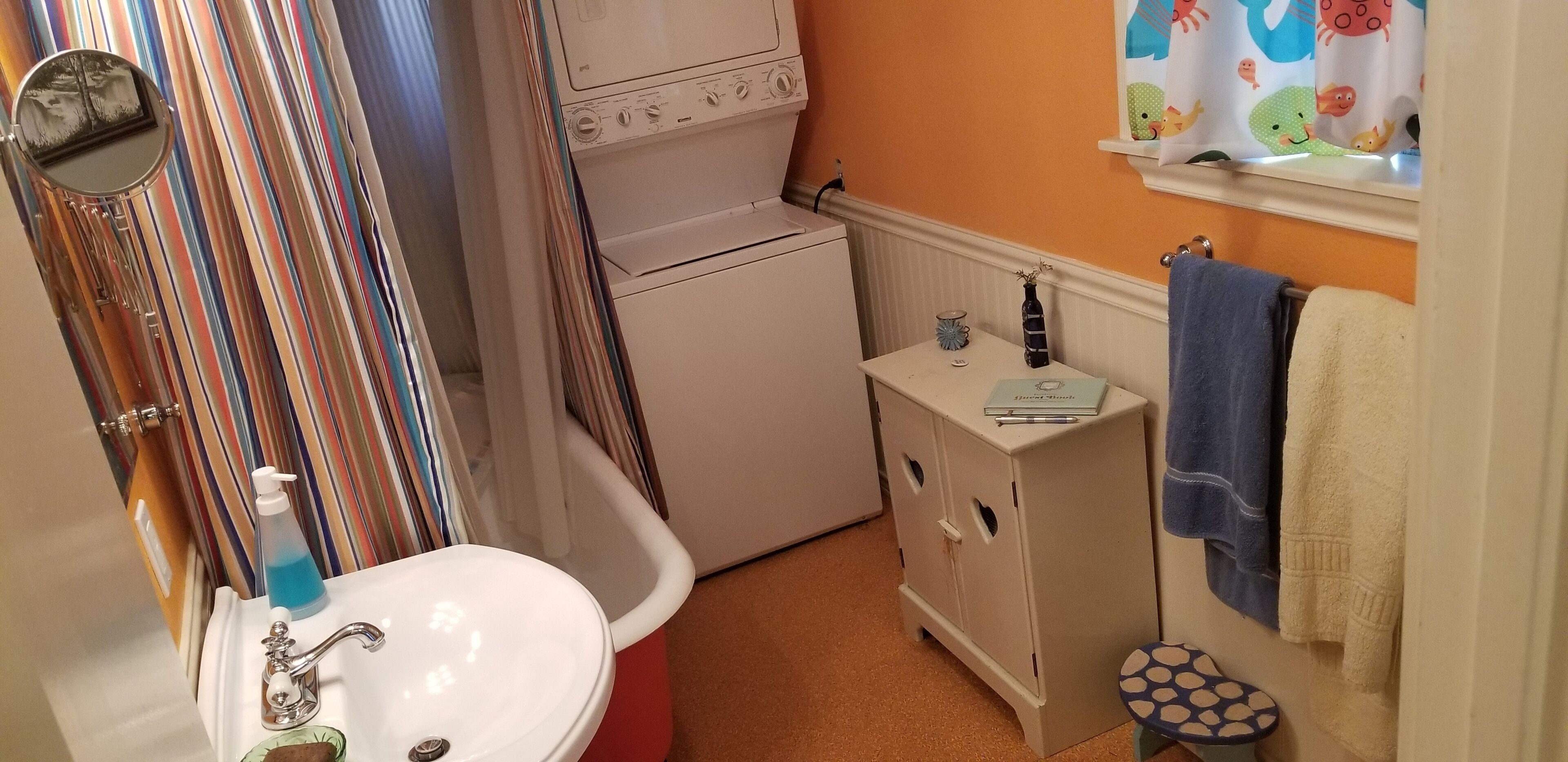 A compact bathroom with a white sink, a red basin, a white washing machine, and a small cabinet with a mirror.