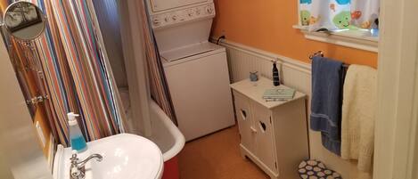 A compact bathroom with a white sink, a red basin, a white washing machine, and a small cabinet with a mirror.