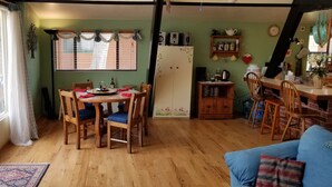 A cozy dining area with a wooden table and chairs, a refrigerator, and a kitchen counter with various items. - Head up to our creek cabin! (Payson)