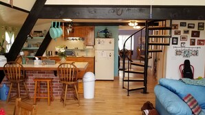 A cozy kitchen with wooden cabinets, a dining area with chairs, a staircase, and a living room with a blue sofa. - Head up to our creek cabin! (Payson)