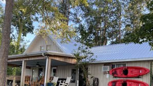 Une maison en bois avec un porche, deux kayaks fixés au mur et un espace extérieur aménagé avec des sièges, protégé par un toit.
