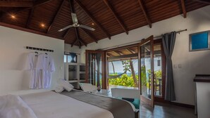 A bedroom with a bed, a ceiling fan, a desk, and a view of the outdoors. - The Tranquilo Lodge (Drake Bay)