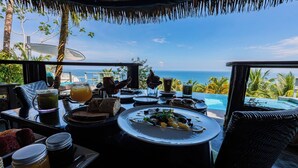 A dining table with plates of food, drinks, and a view of the ocean. - The Tranquilo Lodge (Drake Bay)