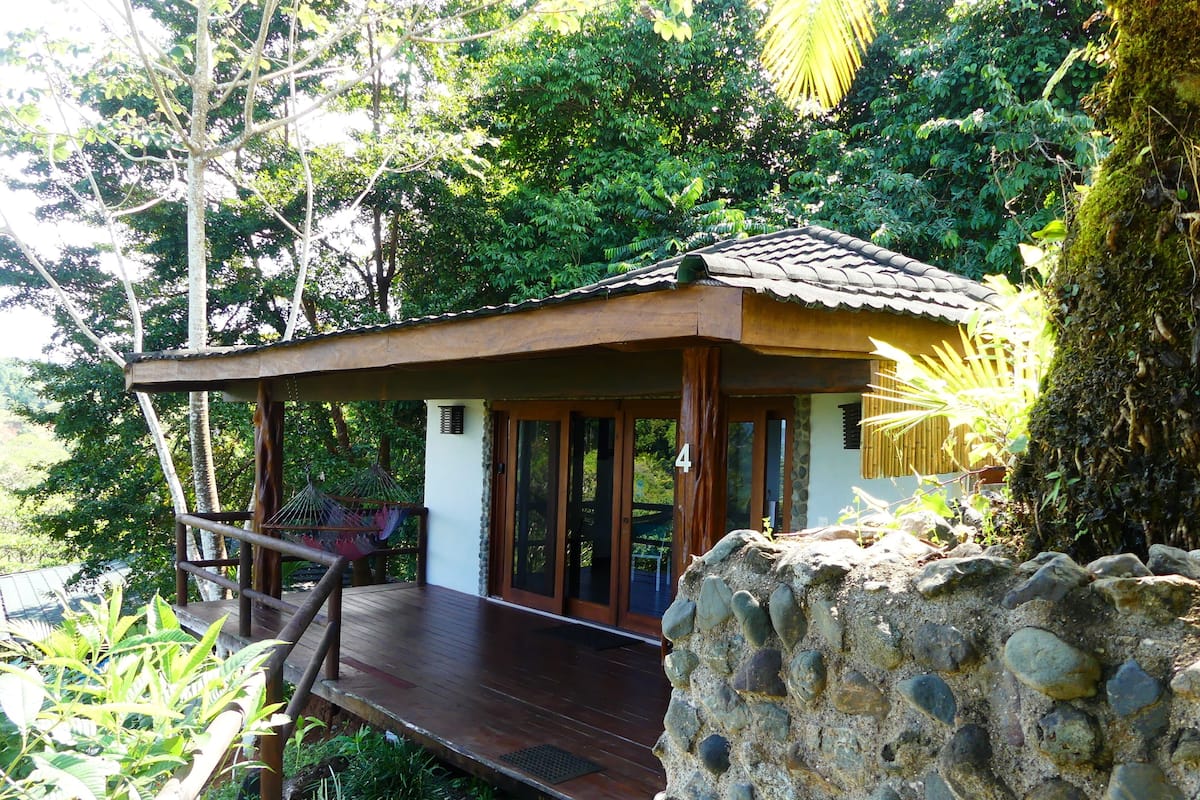 A wooden structure with a tiled roof, a stone wall, and a wooden deck leading to a door.