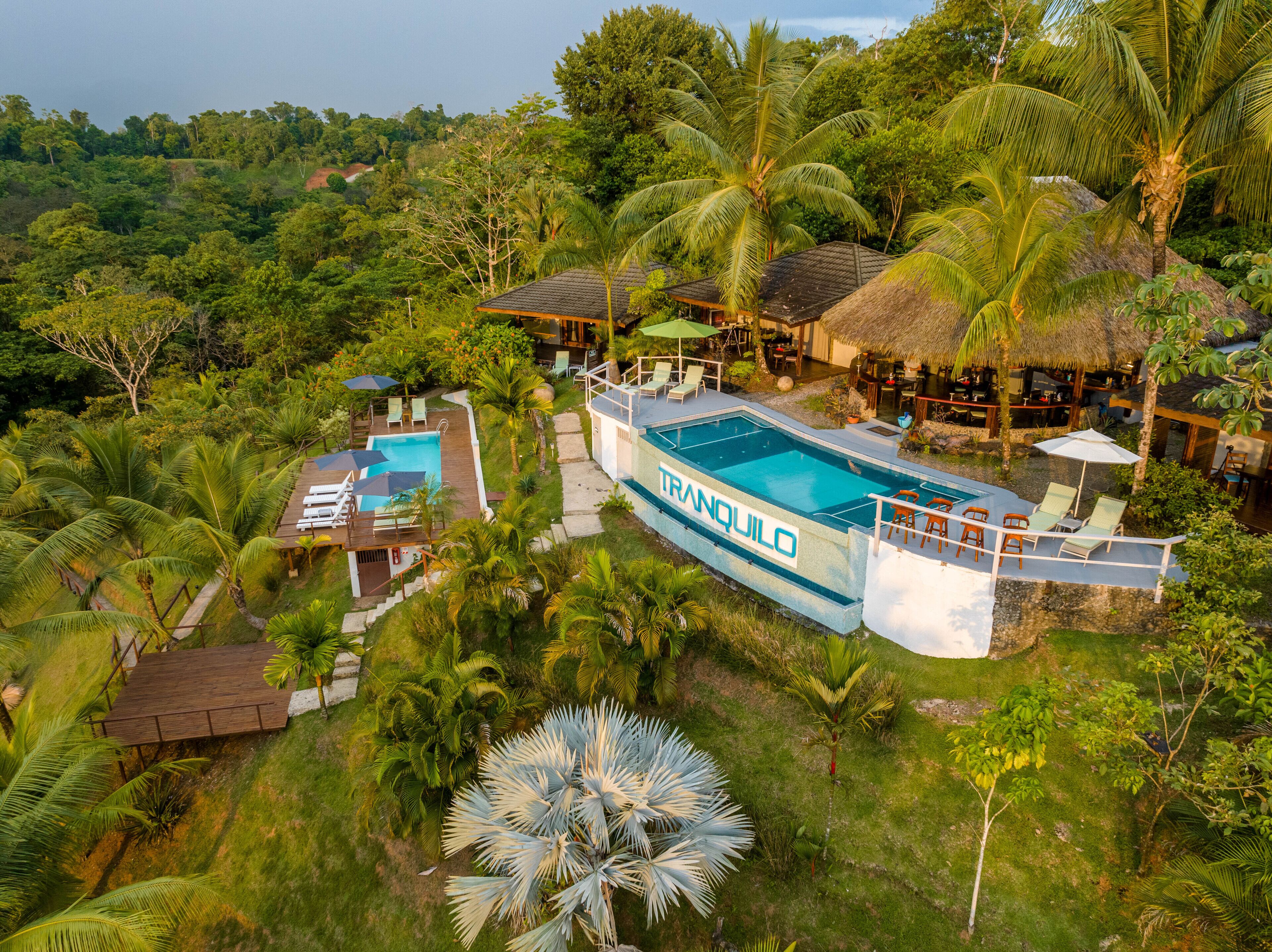 Un resort con una amplia piscina, varias zonas de descanso y exuberante entorno tropical.