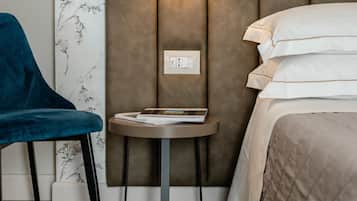 Une chambre d’hôtel avec un lit, une chaise bleue, une petite table avec une lampe et un papier peint à motifs floraux.