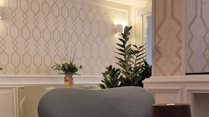 A modern living room with a grey armchair, a floor lamp, and a decorative vase with flowers. - Hotel Du Lac Gardone Riviera (Gardone Riviera)