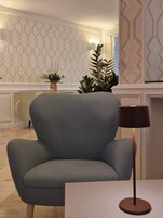 Una sala de estar moderna con un sillón gris, una lámpara de pie y un florero decorativo con flores.